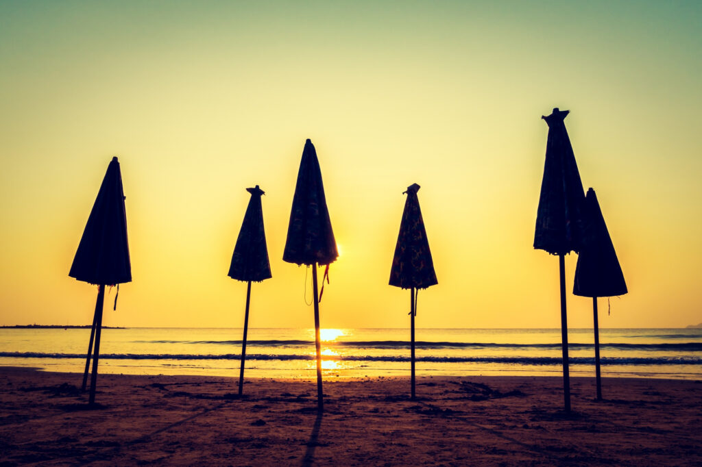 Photo of a beach at sunset with several closed umbrellas standing in the sand.